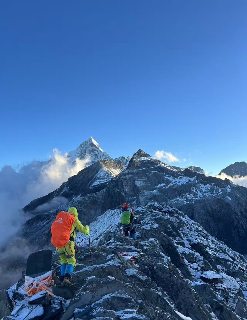 Climbers on the summit ridge of Mount Siguniang with snow-capped peak in distance